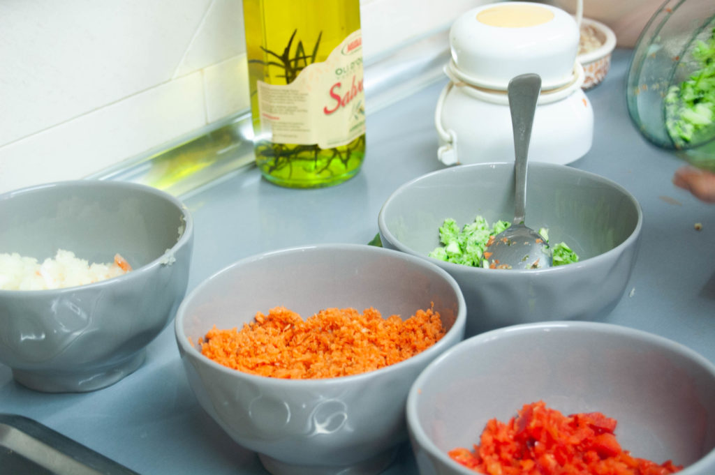 Cuatro cuencos con alguno de los ingredientes para preparar las berenjenas rellenas. Está la zanahoria picada, pimiento rojo y verde y cebolla picada.