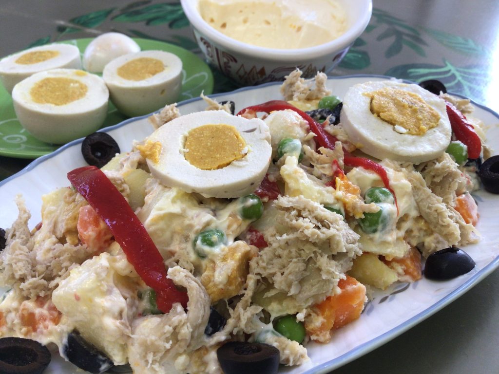 Primer plano de una ración de ensaladilla rusa vegana completa, con su veganesa, sus olivitas negras, su pimiento morrón a tiras, su huevo vegano, su veganatun apetitoso y sus verduritas cocidas.